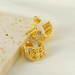 Golden C-shaped chain earrings with inlaid crystals on beige stone background