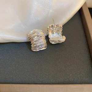 Detailed view of silver wrinkled texture earrings on black tray and white silk