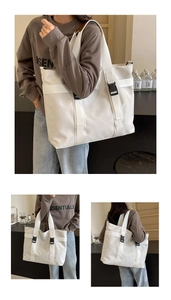 Detail of white canvas tote bag featuring black buckle and adjustable shoulder strap
