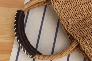 Close-up of woven straw bag with leather wrapped handles and contrast stitching