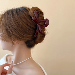 Detail of a large burgundy ribbon bow hair claw clip worn on model's dark brown hair