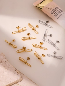 Détail des boucles d'oreilles nœud papillon en fini doré et argenté sur pierre texturée