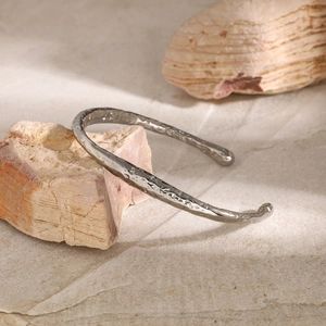 Details des silbernen Edelstahlarmreifs mit Hammerschlag-Textur auf Naturstein-Hintergrund