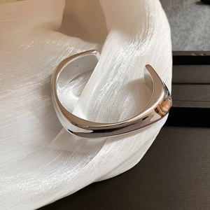 Détail d'un bracelet jonc argenté poli posé sur un tissu en soie blanche chic