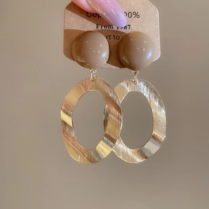 Detail of brushed gold oval drop earrings with brown resin beads on display card