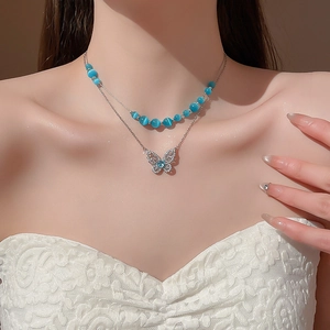 Detailed view of silver butterfly necklace with blue cat eye stone beads on a model