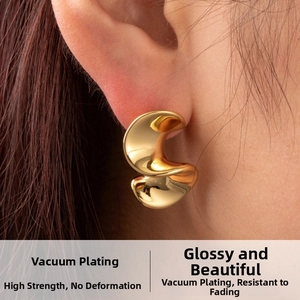 Close-up of golden S-shaped drop earrings with a polished surface and unique wavy texture
