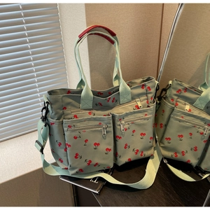 Detailed view of green tote bag with cherry print featuring multiple zipper pockets