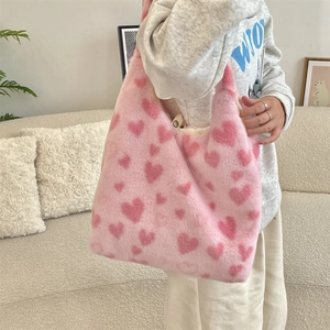 Detail of pink plush tote bag with heart patterns held by a model in a cozy indoor setting