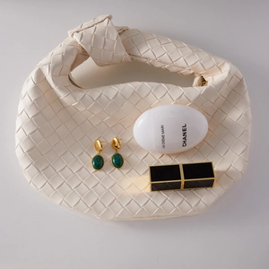 Detail of luxury gold earrings with green resin pendants next to an ivory woven handbag