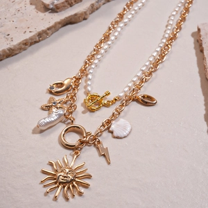 Detail of layered gold chain necklace featuring sun face charms and freshwater pearls