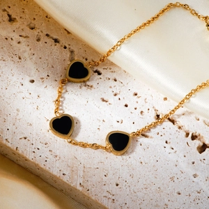 Elegant gold chain bracelet with three black heart pendants on a textured stone base