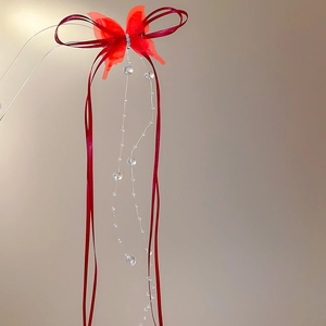 Detail of red butterfly hair clip featuring crystal tassels and silk ribbons on a soft background