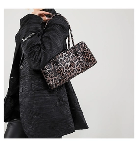 Detail of a stylish leopard print shoulder bag worn with a luxury black coat on a model