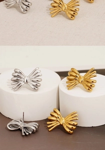 Detail of silver and gold plated bow stud earrings showing metallic texture and shape