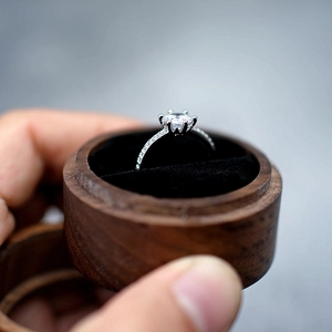 Macro shot of silver ring with round diamond in a dark walnut wood jewelry box