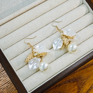 Detailed macro of white petal and pearl earrings on a grey velvet jewelry display box