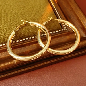 Polished gold round hoop earrings displayed on green velvet and wooden frame detail