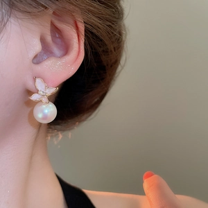 Détail de boucles d'oreilles papillon dorées avec perle portées par un mannequin