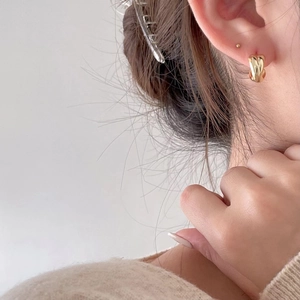 Macro detail of twisted heart stud earrings in gold finish worn by model on ear