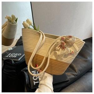 Detail of woven straw tote bag featuring bicolor design and lace floral ribbon bow