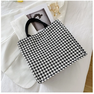 Detail of black and white houndstooth tote bag with round handles on white background