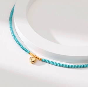 Exotic turquoise beaded necklace with golden heart pendant on white minimalist display