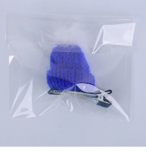 Close-up of blue knitted mini hat hair clip with a white pompom in clear packaging