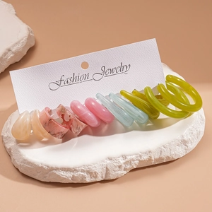 Close-up of a 12-piece colorful resin earring and ring set on white marble display