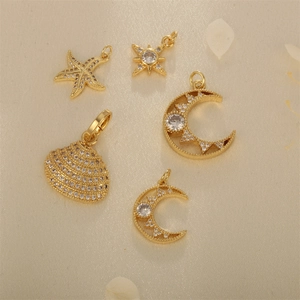 Gold-plated brass pendants with zirconia in starfish, moon, and shell shapes on beige fabric