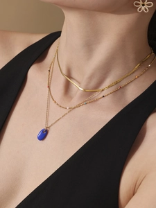 Nahaufnahme mehrlagiger Goldketten mit blauem Emaille-Anhänger und Blumen-Ohrsteckern