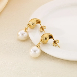 Detail of gold hammered metal earrings with round pearls on white ceramic tray