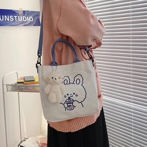 Detail der weißen Canvas-Tasche mit Hasen-Illustration, Plüsch-Anhänger und blauem Gurt