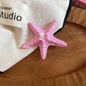 Detailed close-up of a pearlescent pink starfish hair clip on a wavy wooden tray