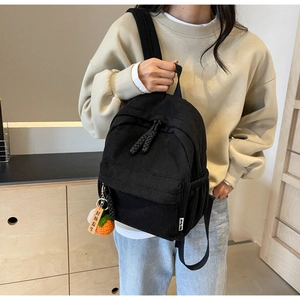 Detail of black corduroy backpack with custom persimmon pendant and dual zipper closure