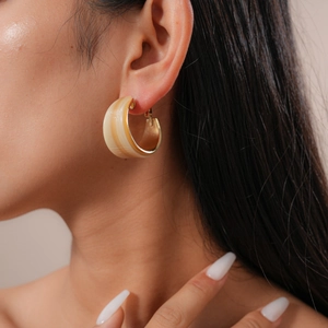 Close-up of a wide beige resin C-shape earring with gold metallic lining on a model