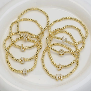 Golden stretch bead bracelet featuring cubic zirconia bubble letter alphabet pendants