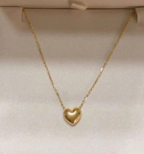 Detailed top view of a polished 18K gold heart pendant necklace in a beige jewelry box