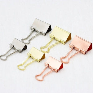 Set of six metal binder clips in gold, silver and rose gold on white wood background