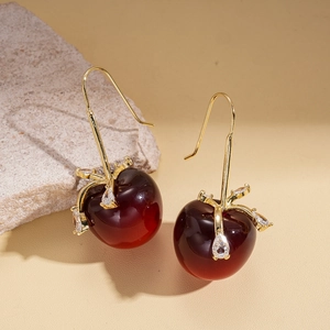 Boucles d'oreilles cerises rouges avec feuilles dorées et zircons sur pierre claire
