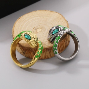 Polished gold and silver snake rings with green eyes and enamel scales on wood