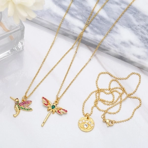 Detailed view of gold hummingbird and dragonfly necklaces with zircons on marble