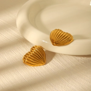 Detailed view of heart earrings with linear texture in warm light on ceramic tray