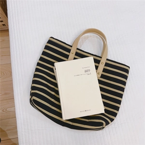 Detail of striped canvas tote bag with leather handles and bronze rivets on white background