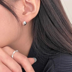 Close-up of a model wearing silver round stud earrings and a textured braided open ring