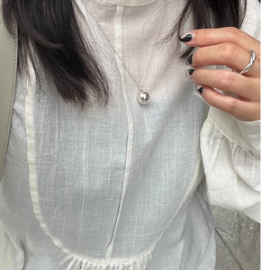 Close-up of minimalist silver ball pendant necklace and twisted ring on female model