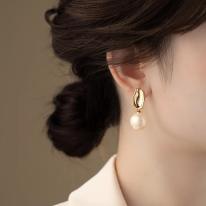 Elegante goldene Hammerschlag-Ohrringe mit Perlen, getragen von einem Model im Licht