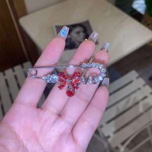 Detail of silver safety pin brooch with red rhinestone bow and crystal LOVE charm