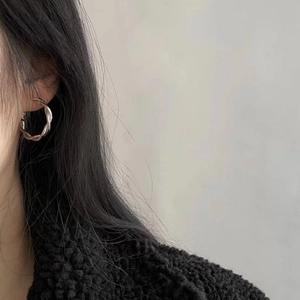 Detail of silver twisted hoop earrings worn by a model in a black textured coat