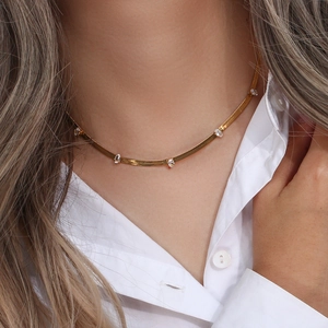Macro detail of gold-plated flat snake chain necklace with clear zircon stones on a model